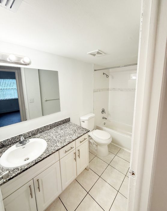Modern bathroom with elegant granite countertop, sleek white cabinetry, and a combined bathtub and shower.