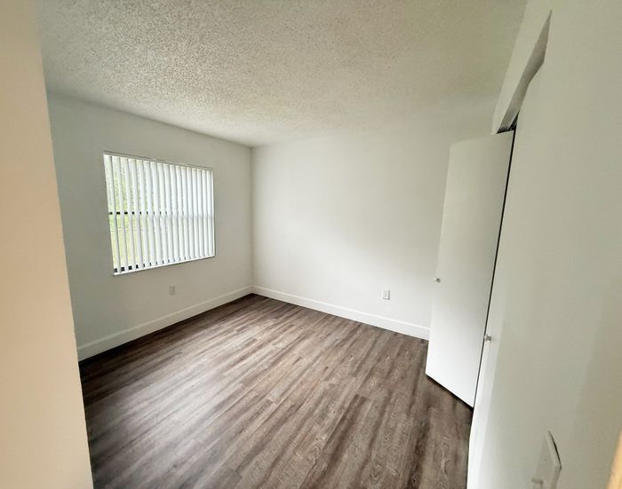 Bright, empty bedroom with large window and modern wood flooring, ready for personal touch.