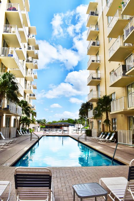 Inviting outdoor pool area nestled between modern apartment buildings with balconies, perfect for relaxation under a bright blue sky.