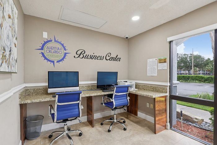 Inviting business center with modern computers, sleek blue chairs, and natural light at Aventura Orlando Apartments, ideal for productivity and comfort.