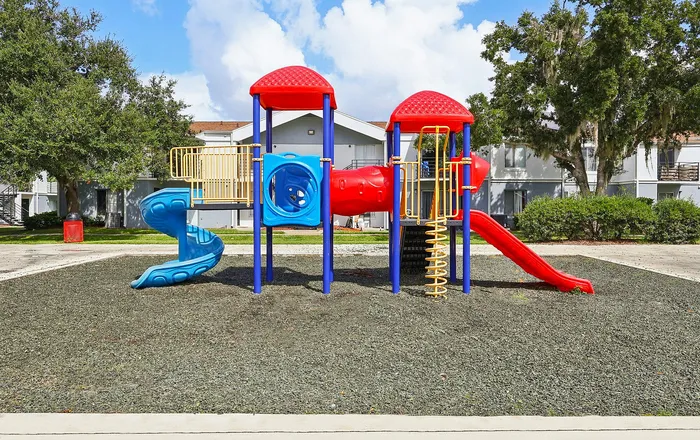 Vibrant community playground with colorful slides and climbing structures, set in a lush green courtyard, perfect for family fun and outdoor activities.