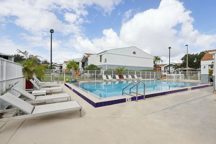 Inviting community pool area with modern lounge chairs, vibrant landscaping, and clear blue skies, perfect for relaxation.