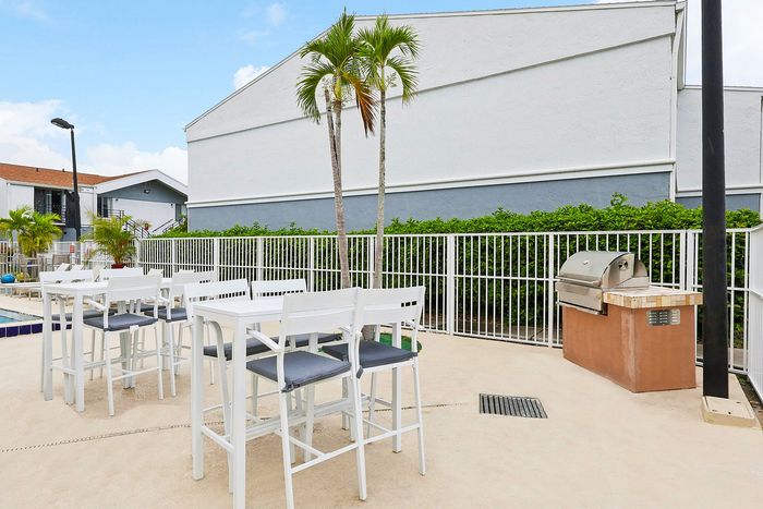 Chic outdoor patio area with modern white dining furniture and a sleek built-in grill, perfect for entertaining in a stylish apartment complex.