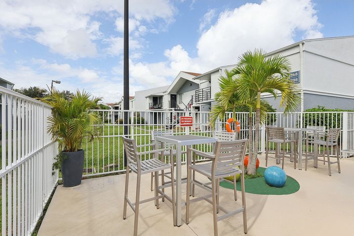 Charming outdoor seating area with modern furniture, lush greenery, and a bright, sunny sky, perfect for relaxation.