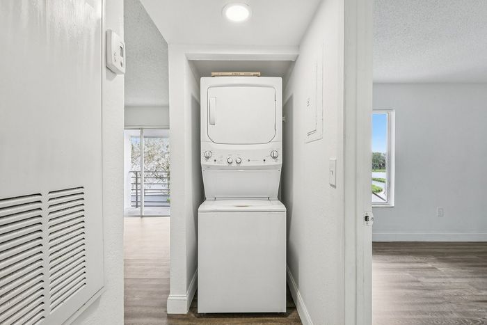 Bright apartment hallway featuring a convenient in-unit stacked washer and dryer, modern flooring, and a glimpse of a sunny balcony view.