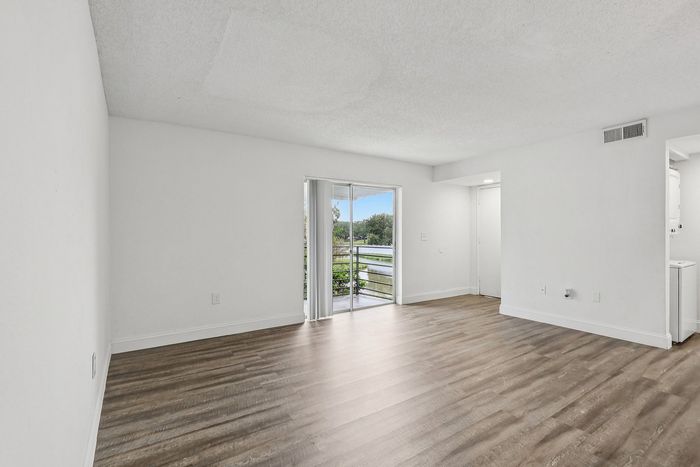 Bright and airy living room with sleek wooden flooring and a large sliding glass door leading to a scenic balcony view.