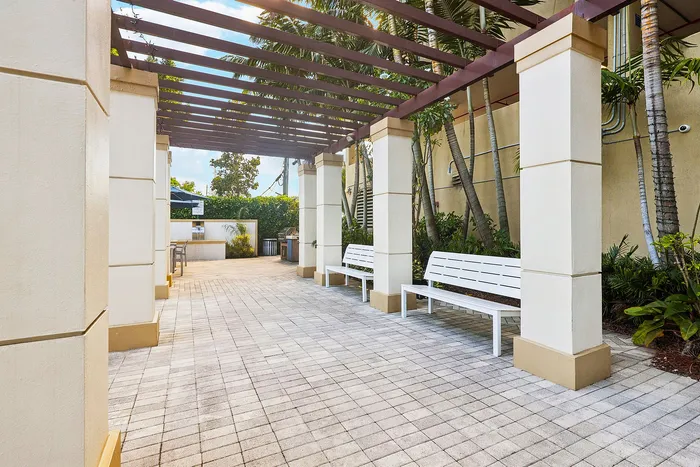 Inviting outdoor common area with pergola-covered walkway, white benches, and lush greenery for relaxation.
