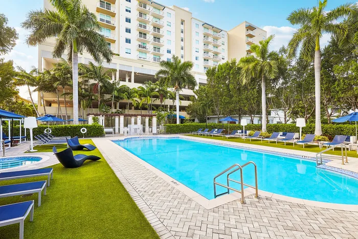 Luxurious apartment complex with a sparkling swimming pool, surrounded by lush palm trees and modern lounge chairs for ultimate relaxation.