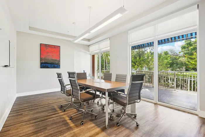 Elegant conference room with modern chairs, wooden table, and large glass doors opening to a lush green view.