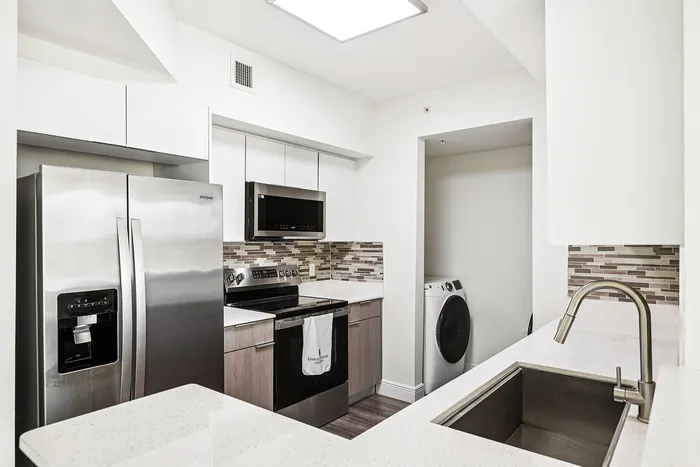 Modern kitchen with stainless steel appliances, sleek countertops, and stylish backsplash, featuring adjacent washer and dryer for convenience.