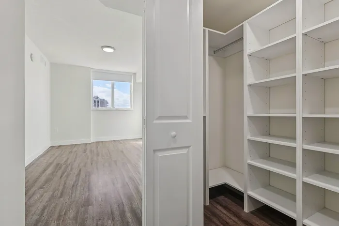 Bright and modern apartment showcasing sleek wooden floors and a spacious walk-in closet with ample shelving.