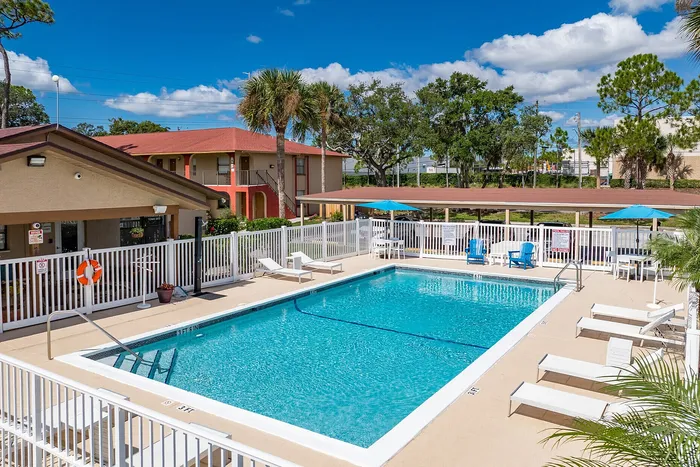 Inviting outdoor pool area with comfortable lounge chairs and vibrant umbrellas, nestled in a lush green setting under a clear blue sky.
