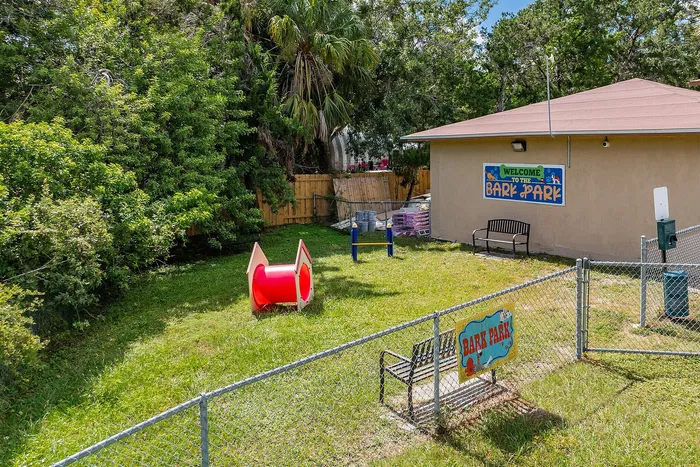 Inviting dog park with agility equipment, shady trees, and a welcoming bench, perfect for playful pets and relaxation.
