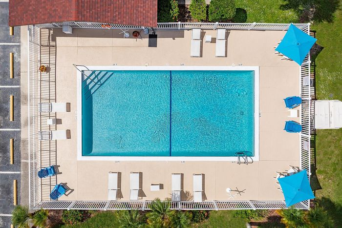 Aerial view of a sparkling blue swimming pool surrounded by luxurious lounge chairs and vibrant blue umbrellas, offering a perfect relaxation spot in a sunny outdoor setting.
