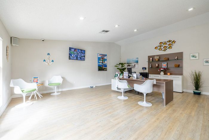 Bright, modern office space featuring sleek white chairs, decorative wall art, and a welcoming reception desk on elegant wooden flooring.
