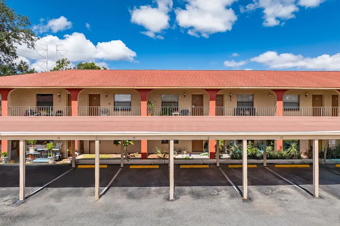 Charming apartment complex with vibrant red roofing, featuring shaded parking and spacious balconies, set against a clear blue sky.