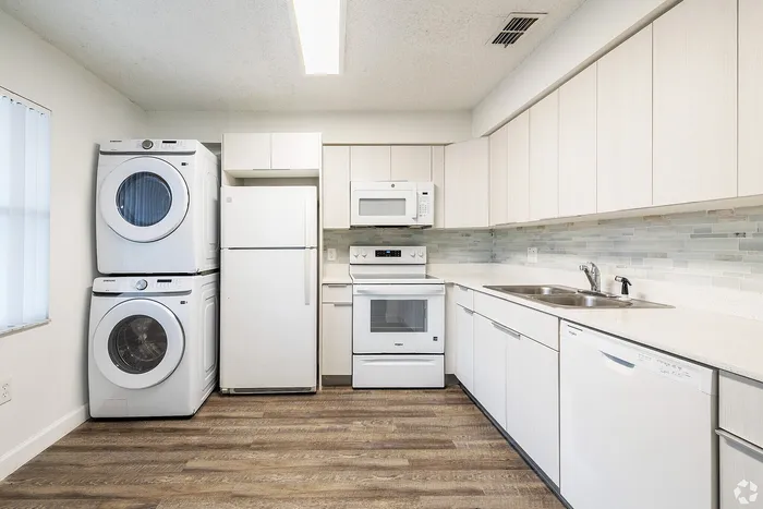Modern kitchen with sleek white cabinetry, built-in appliances, and in-unit washer and dryer in a bright, open space.