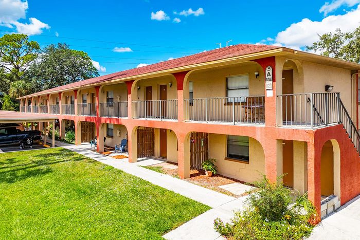Charming two-story apartment building with vibrant red accents, expansive green lawn, and abundant natural light.