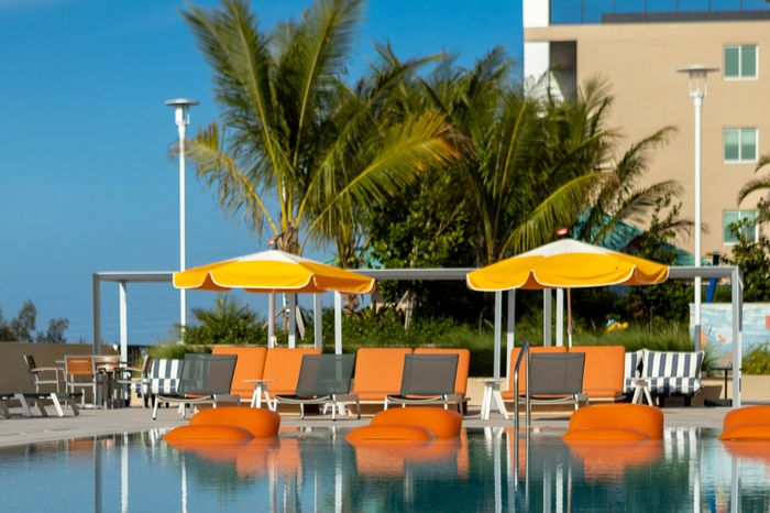 Luxurious outdoor pool area with tropical palm trees, vibrant orange loungers, and sunny yellow umbrellas, perfect for relaxation and enjoyment.