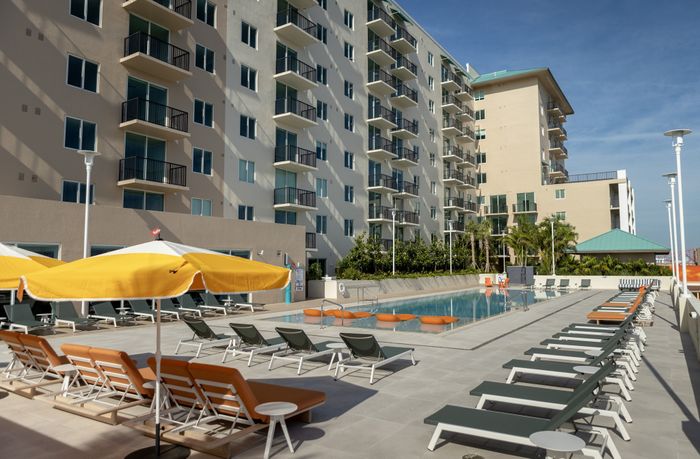 Modern apartment complex with a pristine swimming pool, stylish loungers, and vibrant umbrellas, offering a luxurious outdoor oasis.