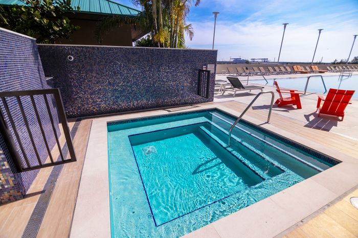 Luxurious rooftop deck featuring a sparkling hot tub, vibrant loungers, and serene pool with a sunny horizon backdrop.