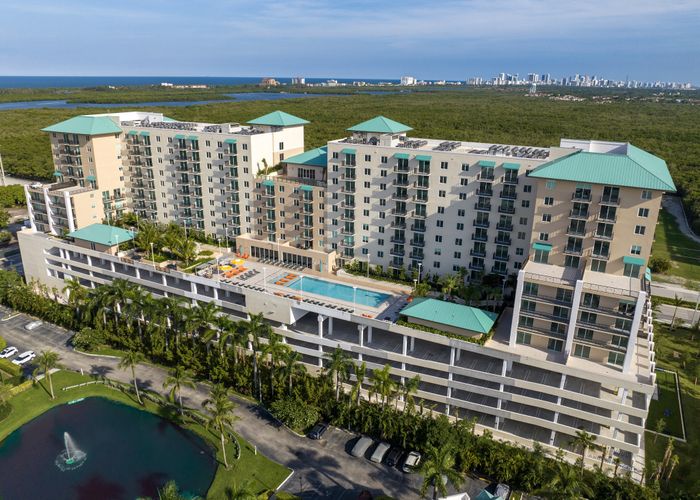Luxurious apartment complex featuring modern design with a rooftop pool, expansive balconies, and panoramic views of lush greenery and city skyline.