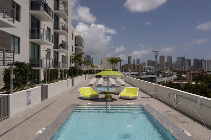 Luxurious rooftop pool terrace with modern lounge chairs, vibrant green umbrellas, and panoramic city skyline views.