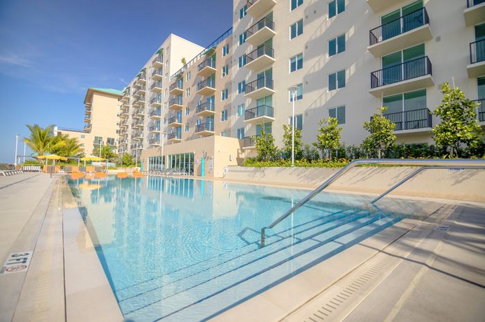 Luxurious apartment complex with a pristine outdoor swimming pool, surrounded by tropical greenery and modern balconies under a clear blue sky.