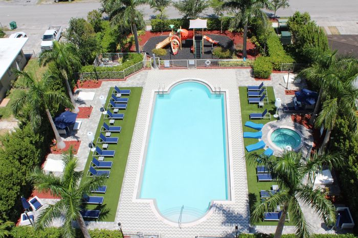 Luxurious aerial view of a sparkling swimming pool and jacuzzi surrounded by lush palm trees and comfortable lounge chairs, perfect for relaxation. Nearby, a vibrant children's playground adds to the family-friendly atmosphere.
