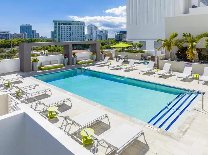 Luxurious rooftop pool area with modern lounge chairs, vibrant greenery, and panoramic city views.