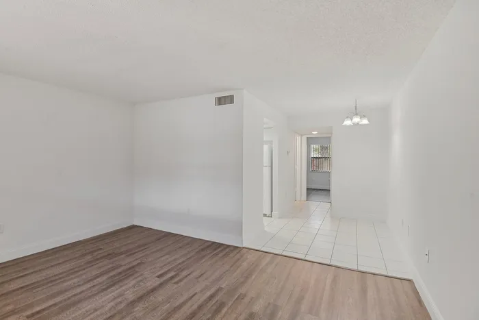 Bright open-concept living space with elegant wood flooring and a modern chandelier, leading to a cozy kitchen area.