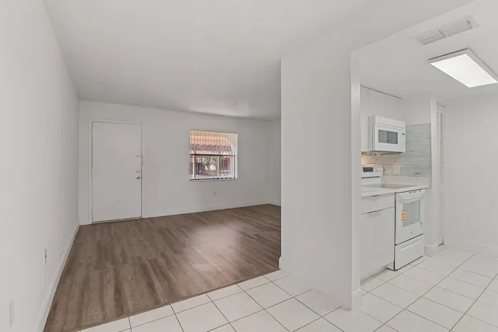 Bright and airy apartment showcasing an open living area with sleek hardwood flooring, adjacent to a modern kitchen with white cabinets and appliances.