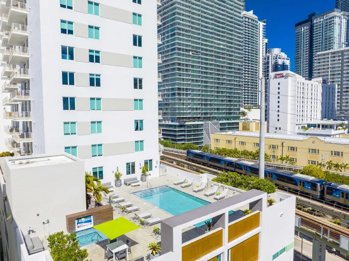 Chic urban apartment complex with a modern pool area, stylish lounge chairs, and vibrant city backdrop.