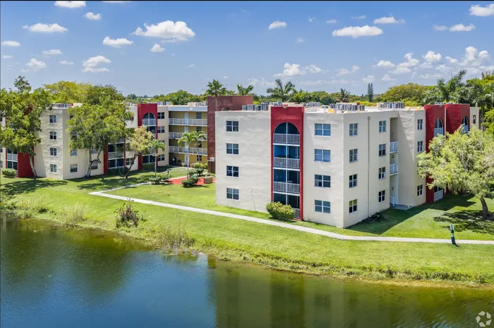 Scenic lakeside apartment complex with vibrant architecture, lush greenery, and clear blue skies.