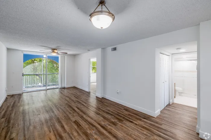 Bright living space with elegant hardwood floors, ceiling fan, and large windows opening to a charming balcony with scenic views.