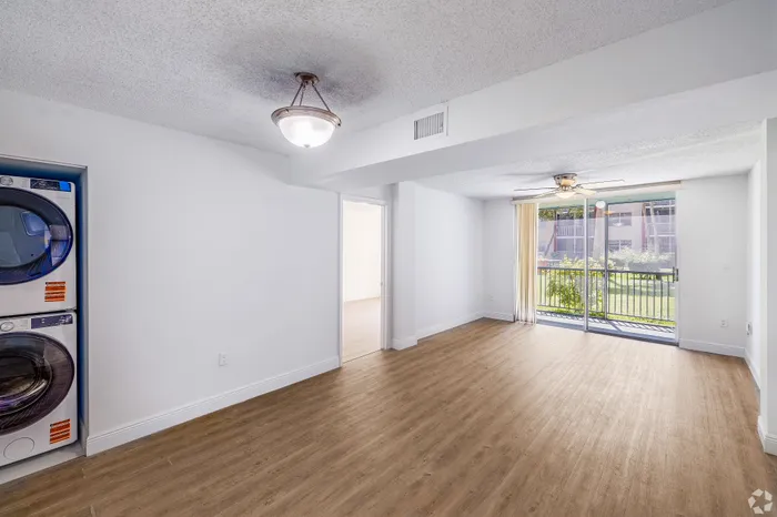 Bright living room with elegant wood flooring, large sliding glass doors to a garden view, and in-unit laundry for modern convenience.