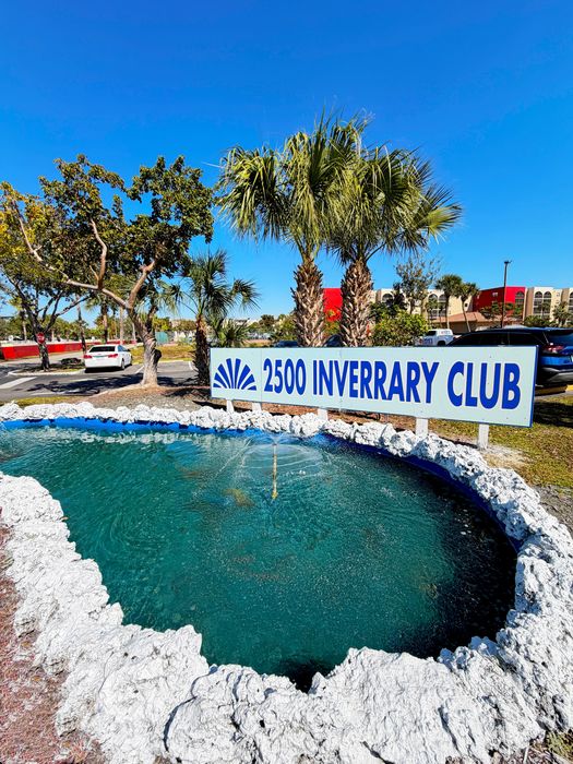 Inviting entrance of 2500 Inverrary Club featuring a serene reflecting pond and elegant landscaping, perfect for a vibrant community ambiance.