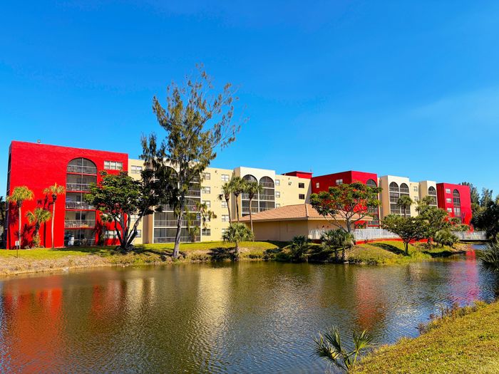 Captivating lakeside apartment complex with vibrant red and cream exteriors, surrounded by lush greenery and scenic water views.