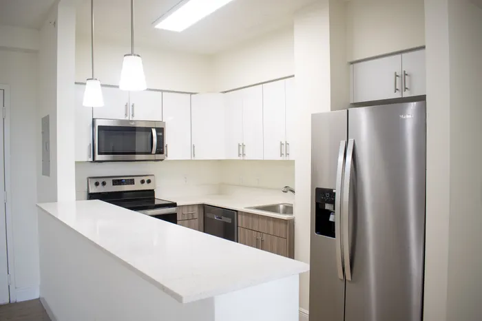 Modern kitchen with sleek stainless steel appliances, elegant white cabinetry, and a spacious countertop illuminated by stylish pendant lights.