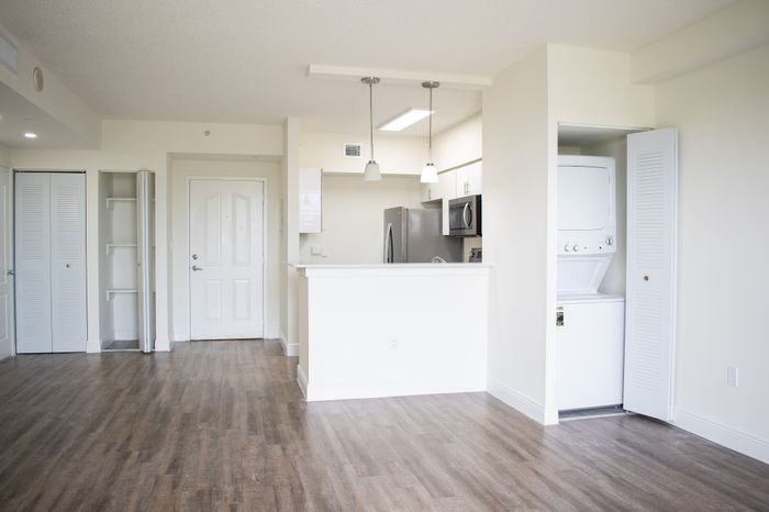 Bright modern apartment entry with sleek kitchen, stainless steel appliances, and in-unit laundry on elegant wood flooring.