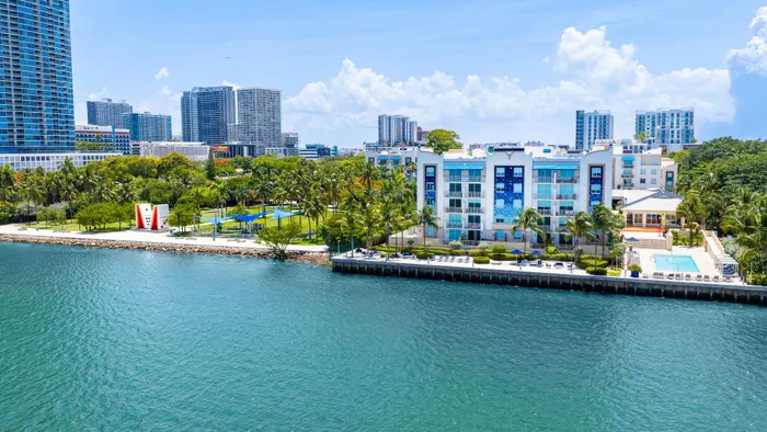 Luxury waterfront apartment complex with vibrant pool area and lush palm trees, offering stunning skyline views.