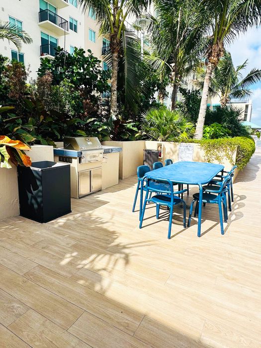 Inviting outdoor patio with a sleek barbecue grill and vibrant blue dining set amidst lush tropical landscaping.