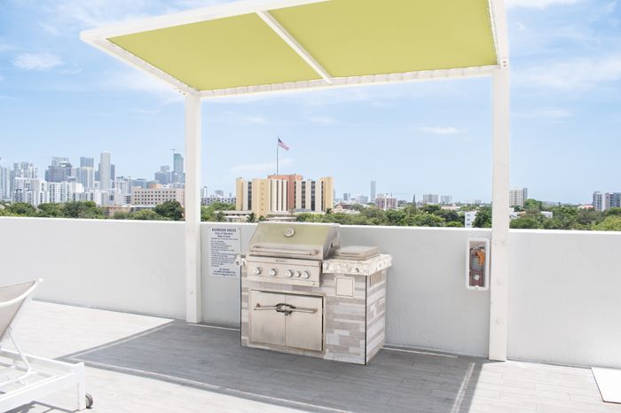 Chic rooftop terrace with a stainless steel BBQ grill, modern canopy, and stunning cityscape views.