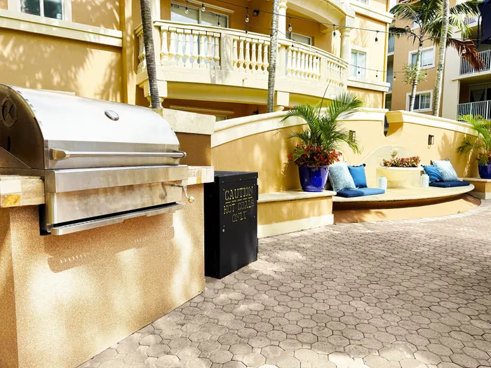 Luxurious outdoor patio featuring a modern stainless steel grill, elegant seating with plush cushions, vibrant potted plants, and a charming decorative fountain, set against a stunning apartment facade.