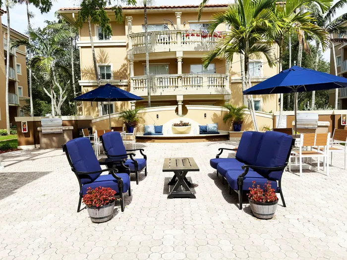 Charming outdoor patio with elegant seating and umbrellas, surrounded by lush tropical plants and a stylish apartment building backdrop.