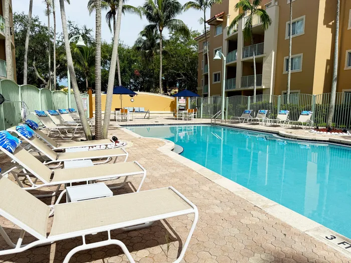 Inviting outdoor pool area with sun loungers and tropical palm trees at a modern apartment complex.
