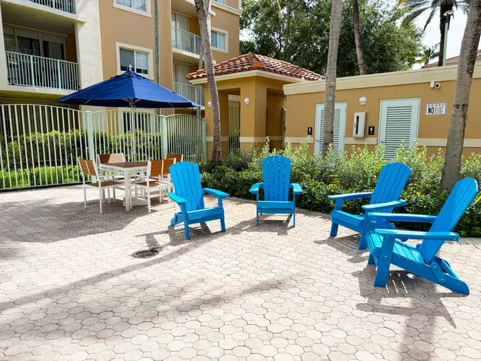 Charming patio space with bright blue Adirondack chairs and a cozy dining set under a navy umbrella, perfect for outdoor relaxation and gatherings.