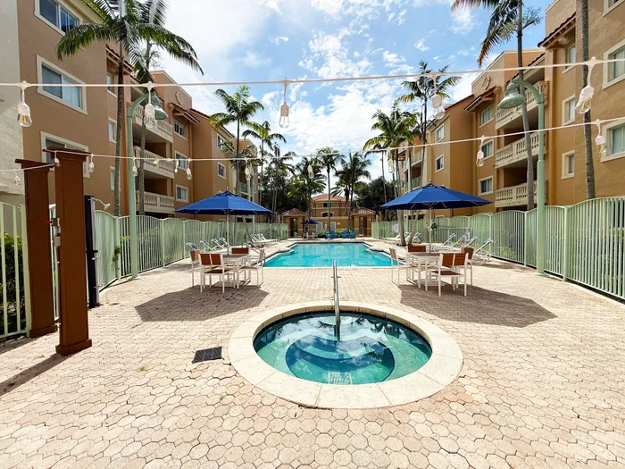 Inviting apartment complex with a sparkling swimming pool, surrounded by lush palm trees and cozy seating areas, perfect for relaxation.