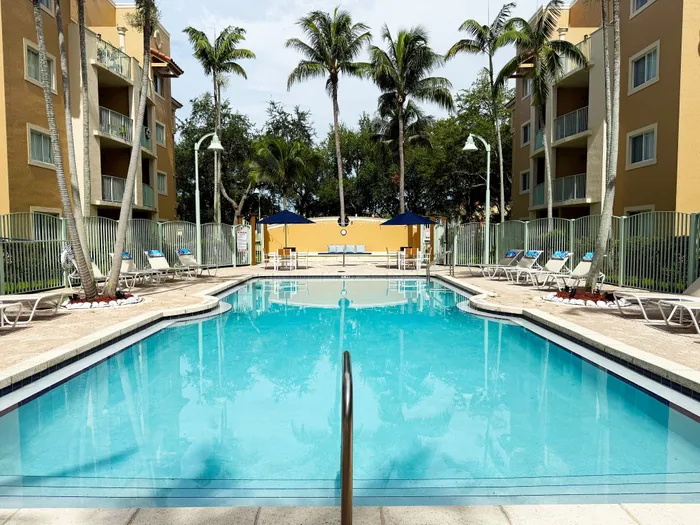 Inviting outdoor swimming pool with sun loungers, surrounded by palm trees and modern apartments in a tropical setting.
