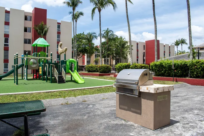 Vibrant apartment community featuring a modern playground and outdoor grill area bordered by lush palm trees.